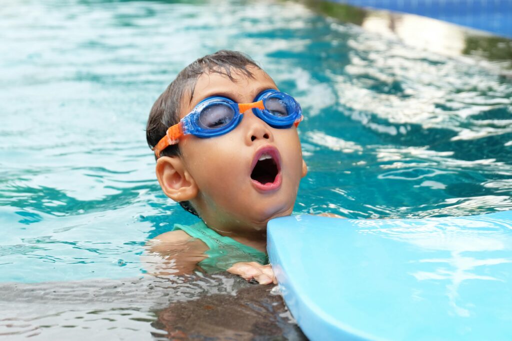 Young child swimming in a pool wearing blue goggles, enjoying summer.